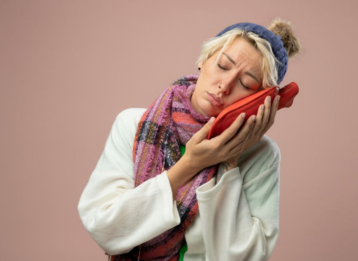 Foto de uma mulher realizando muma compressa morna ou bolsa de água quente na região do ouvido para alivar dor de ouvido e otite